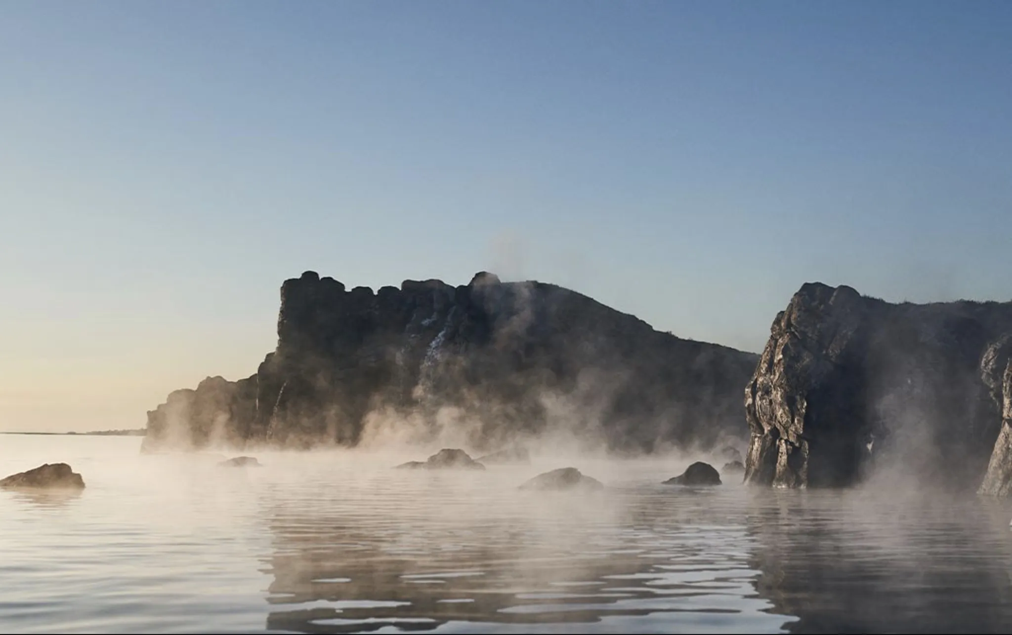 Steaming geothermal waters at Sky Lagoon in Kópavogur with dark rock formations and ocean views.