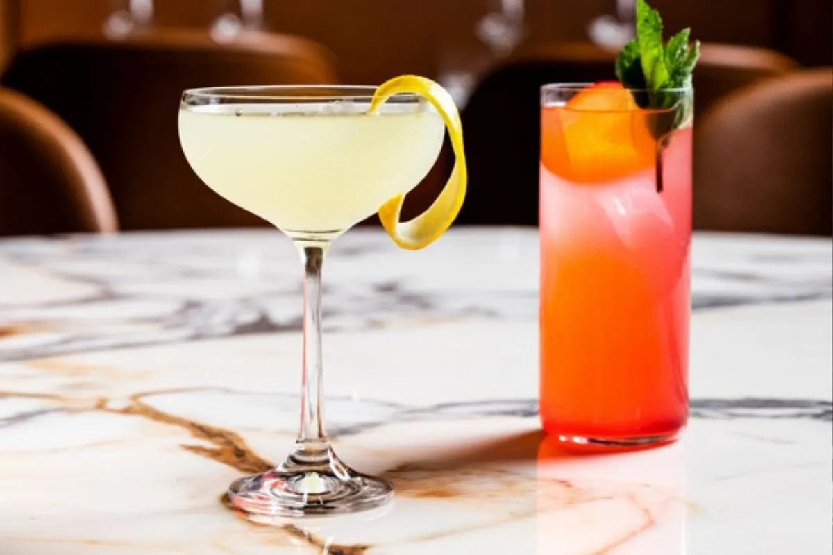 Two colorful craft cocktails—a yellow coupe with lemon twist and a pink highball with mint—at OTO Restaurant Reykjavik.