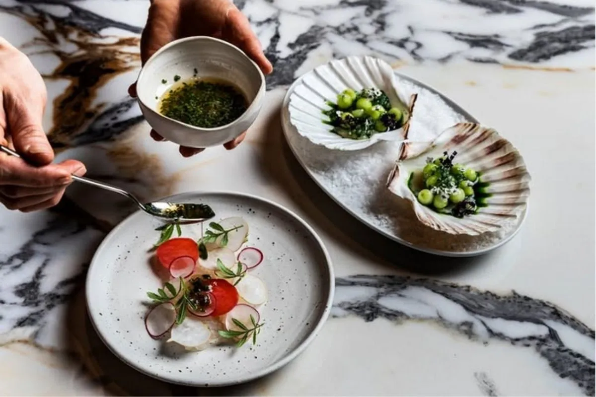 Chef plating scallop crudo with radishes and herb oil at OTO Restaurant in a marble dining setting.