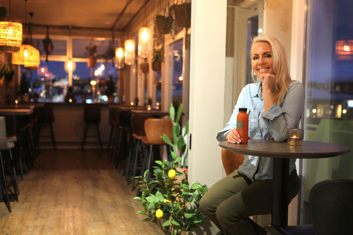 Ingibjörg, the owner of Pure Deli, sitting in the cozy, warm-lit cafe interior in Kópavogur.