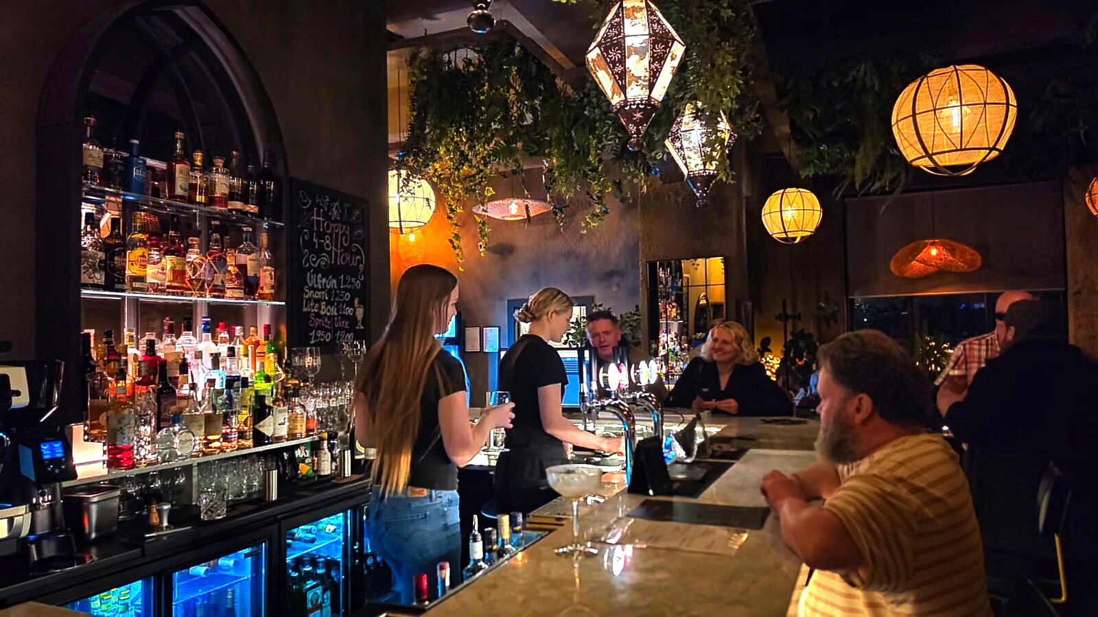 Bartenders serving guests at the bar with a happy hour board