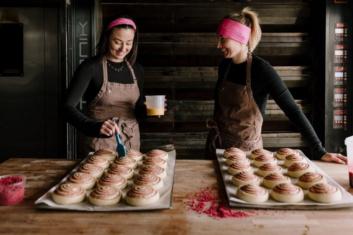 Two bakers at Brauð & Co. glazing trays of signature organic cinnamon rolls.