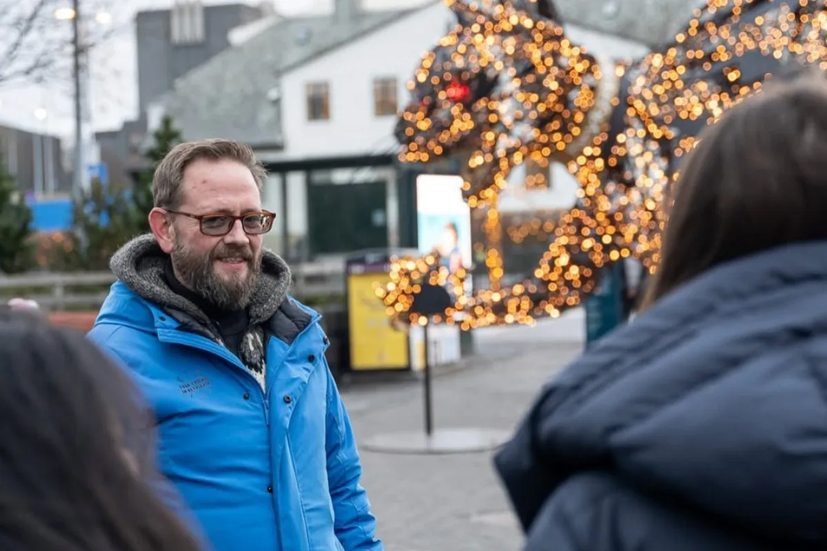 Your Friend in Reykjavik tour guide in a blue jacket in front of the glowing Yule Cat (Jólakötturinn) light display downtown.