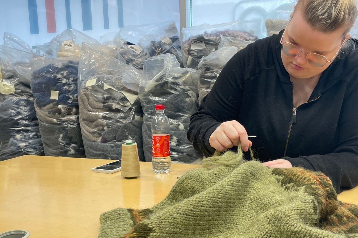 A knitter hand-sewing a green Icelandic wool sweater at The Handknitting Association of Iceland.