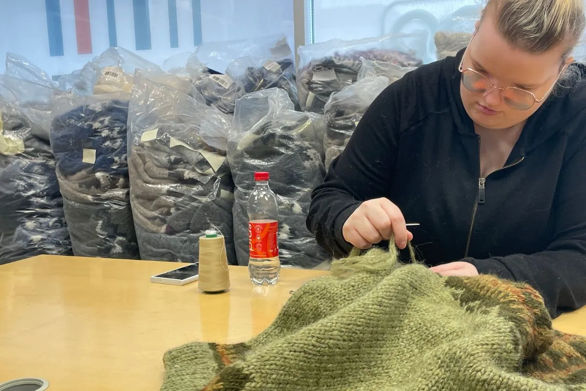 A knitter hand-sewing a green Icelandic wool sweater at The Handknitting Association of Iceland.
