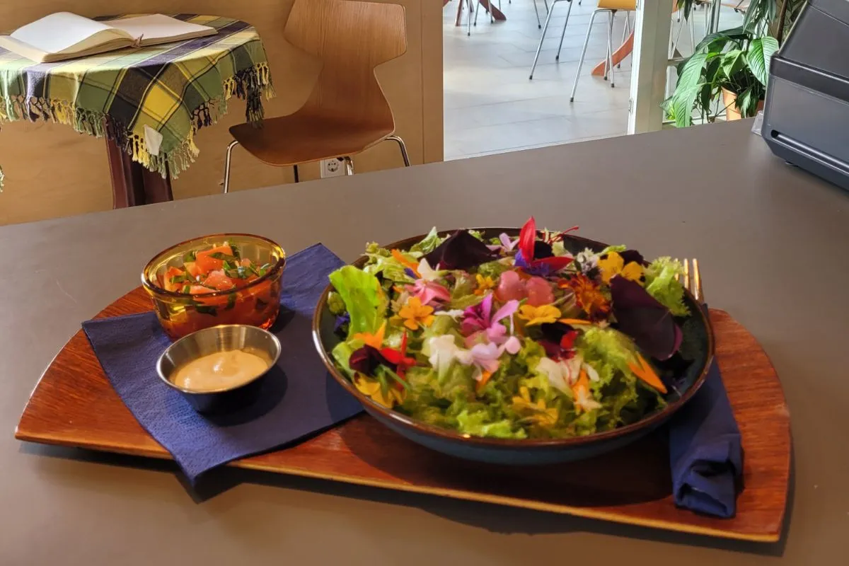 A colorful garden salad topped with edible flowers served on a wooden tray at Hjá Góðu Fólki.