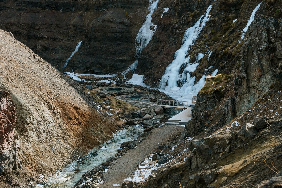 View of geothermal pools in a canyon next to a stream and icy waterfalls.