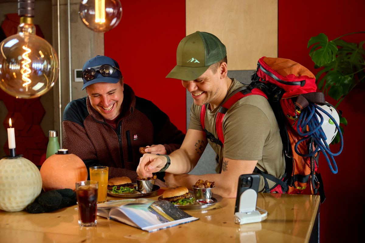 Two hikers with backpacks enjoying burgers and drinks inside Midgard Restaurant in Hvolsvöllur, South Iceland.