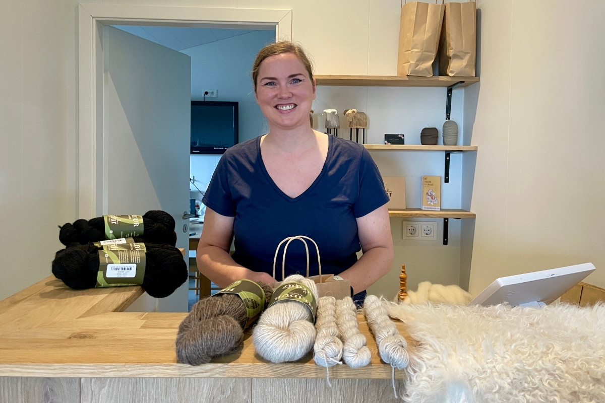 Urður shop owner behind the counter with wool yarn displays.