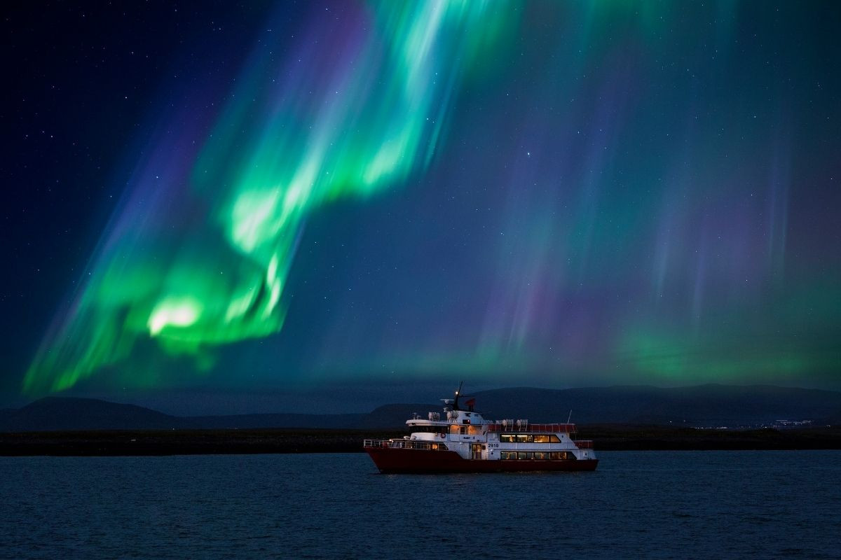 Elding Northern Lights cruise boat in Reykjavik with passengers viewing the green Aurora Borealis over the Icelandic sea.