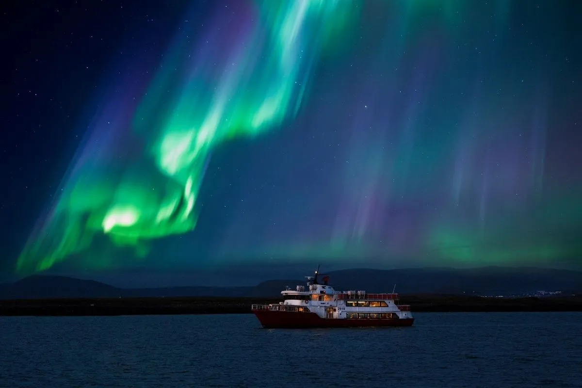 Elding Northern Lights cruise boat in Reykjavik with passengers viewing the green Aurora Borealis over the Icelandic sea.