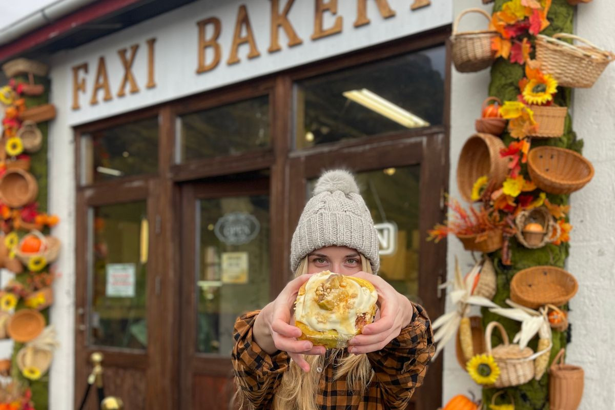 A frosted cinnamon roll outside the decorated storefront of Faxi Bakery in Hvolsvöllur, recommended by Handpicked Iceland.