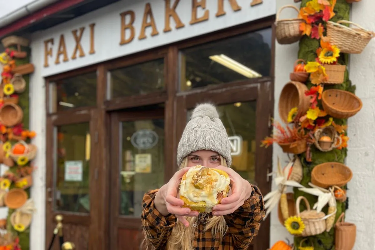 A frosted cinnamon roll outside the decorated storefront of Faxi Bakery in Hvolsvöllur, recommended by Handpicked Iceland.