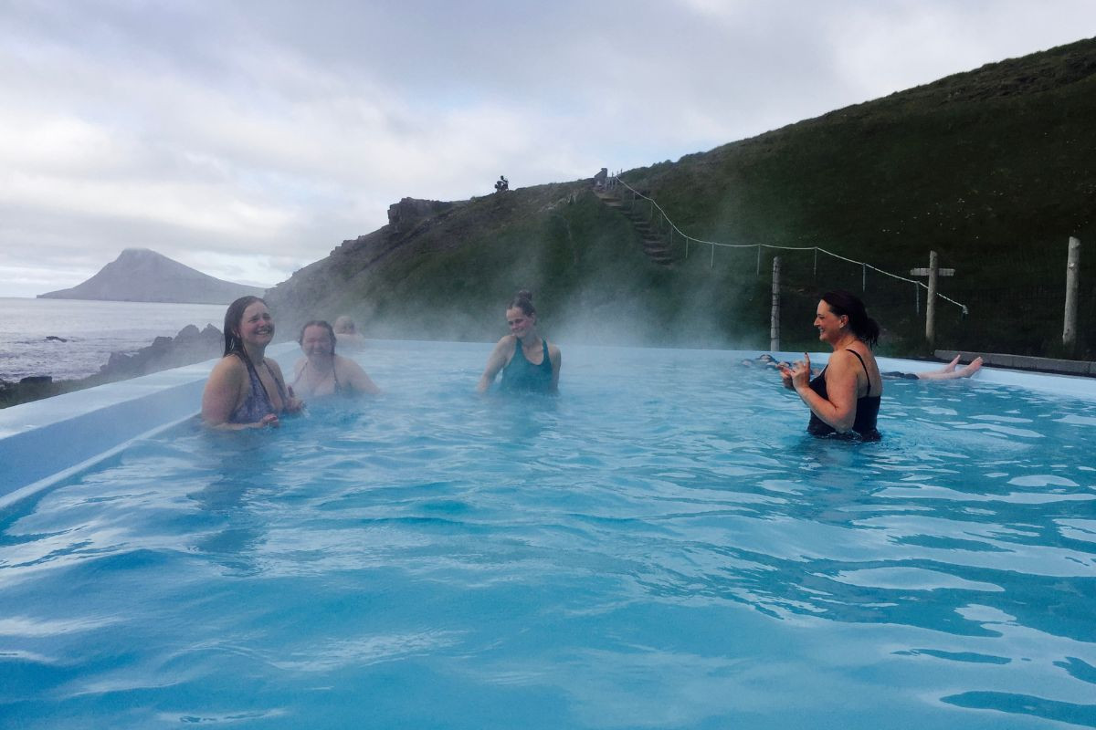 Tourists swimming in the Krossneslaug infinity pool overlooking the ocean in the Westfjords.