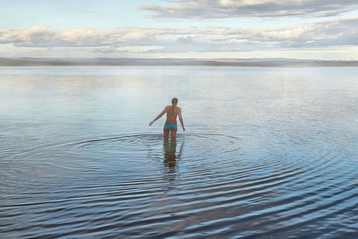 A person wading into the calm waters of Lake Laugarvatn at Fontana baths.
