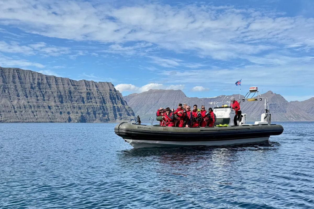 Tourists in red safety suits on a Fjarðaferðir RIB boat enjoying a scenic fjord tour in East Iceland, recommended by Handpicked Iceland.