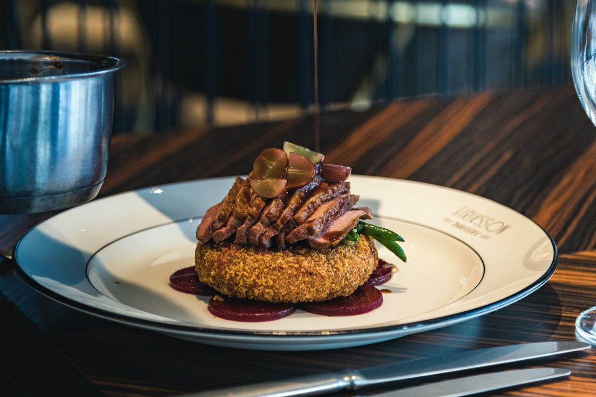 Sauce being poured over a plated duck breast entree served on a crispy potato cake at Eiriksson Brasserie in Reykjavik, Iceland.