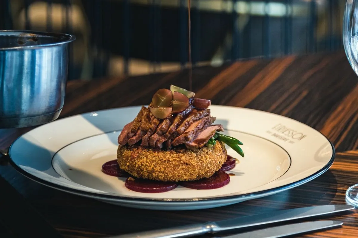 Sauce being poured over a plated duck breast entree served on a crispy potato cake at Eiriksson Brasserie in Reykjavik, Iceland.