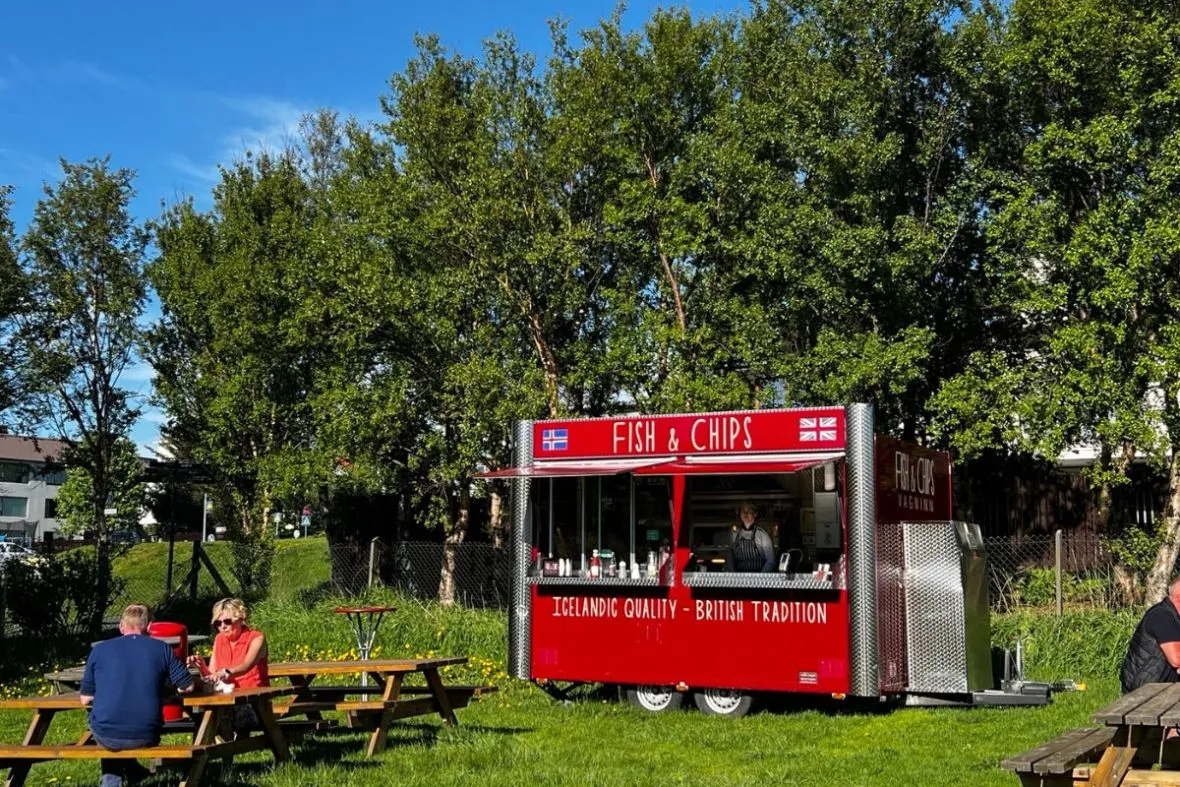 The red Fish and Chips Vagninn food truck in Laugardalur park, surrounded by green trees under a bright blue sky.