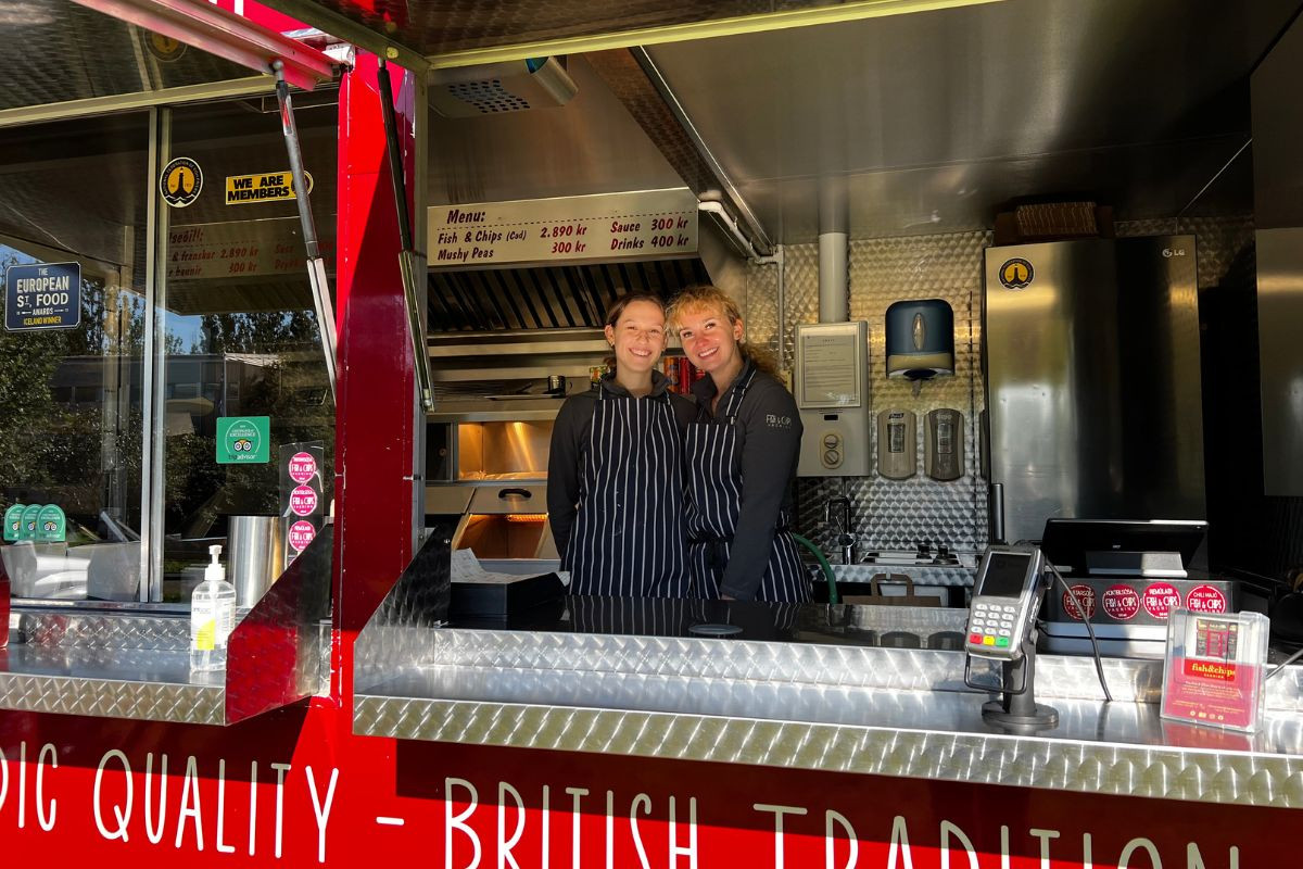 Two smiling workers inside the Fish and Chips Vagninn food truck in Laugardalur, showing the menu and ordering counter.