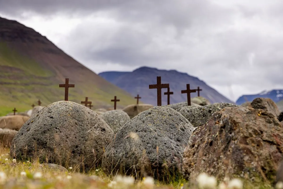 Historic stone graves marked with iron crosses in a green valley near Varmahlíð.