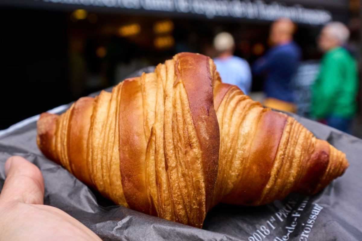 Freshly baked French croissant held by hand at Bar à Croissant in Ísafjörður, Westfjords.