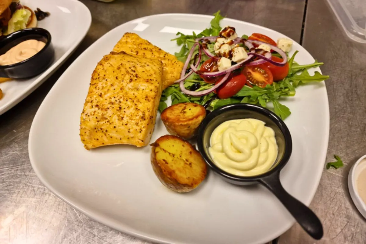 A plate of pan-fried fish served with roasted potatoes, garlic sauce, and a fresh side salad at Bragðavellir barn restaurant.