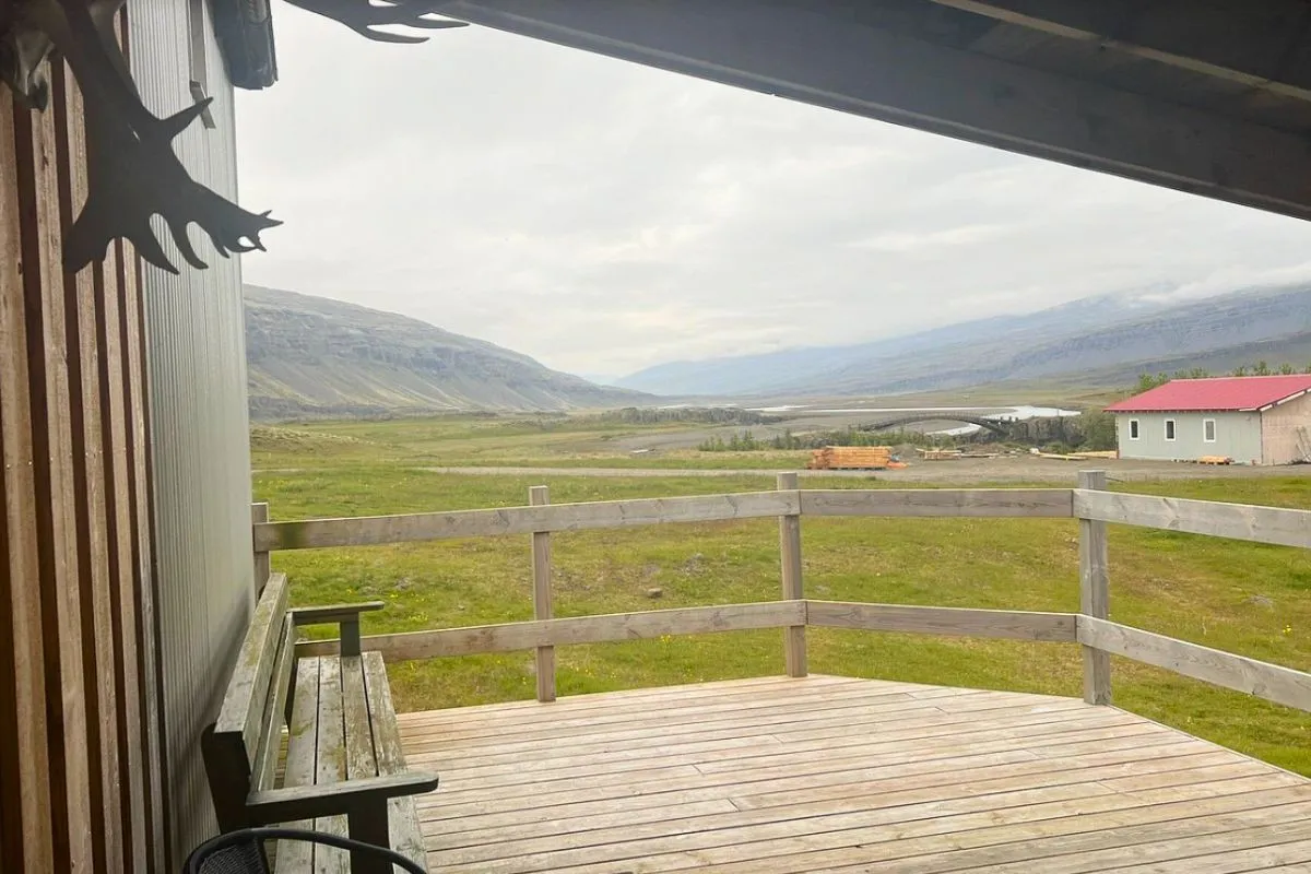 View of a green valley and mountain ranges from a wooden deck with a bench at Bragðavellir Cottages & Restaurant.