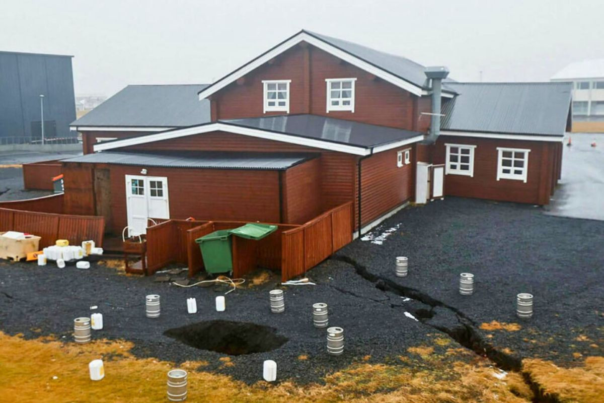 Ground cracks and sinkholes in a gravel yard next to a brown wooden building with Discover Grandavik.