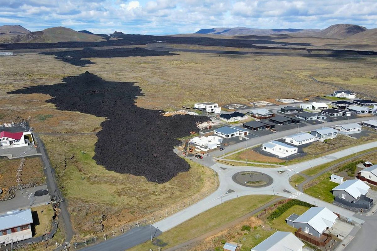Aerial view of a dark cooling lava flow reaching the edge of a residential neighborhood in Grindavík.