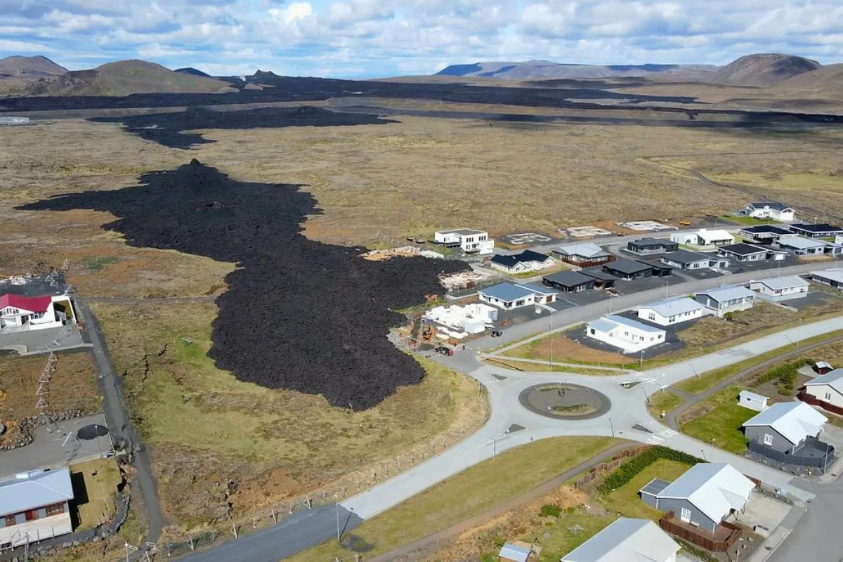 Aerial view of a dark cooling lava flow reaching the edge of a residential neighborhood in Grindavík.