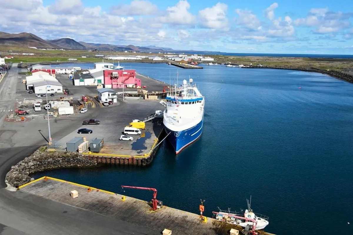 View of a large blue fishing vessel docked at the Grindavík harbor pier under a blue sky.