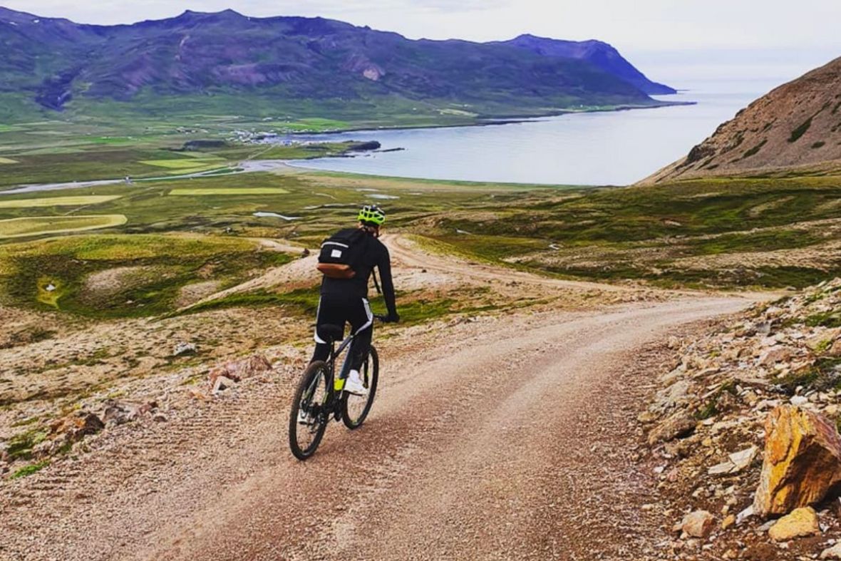 Cyclist riding down a gravel mountain trail toward the scenic coast in East Iceland.