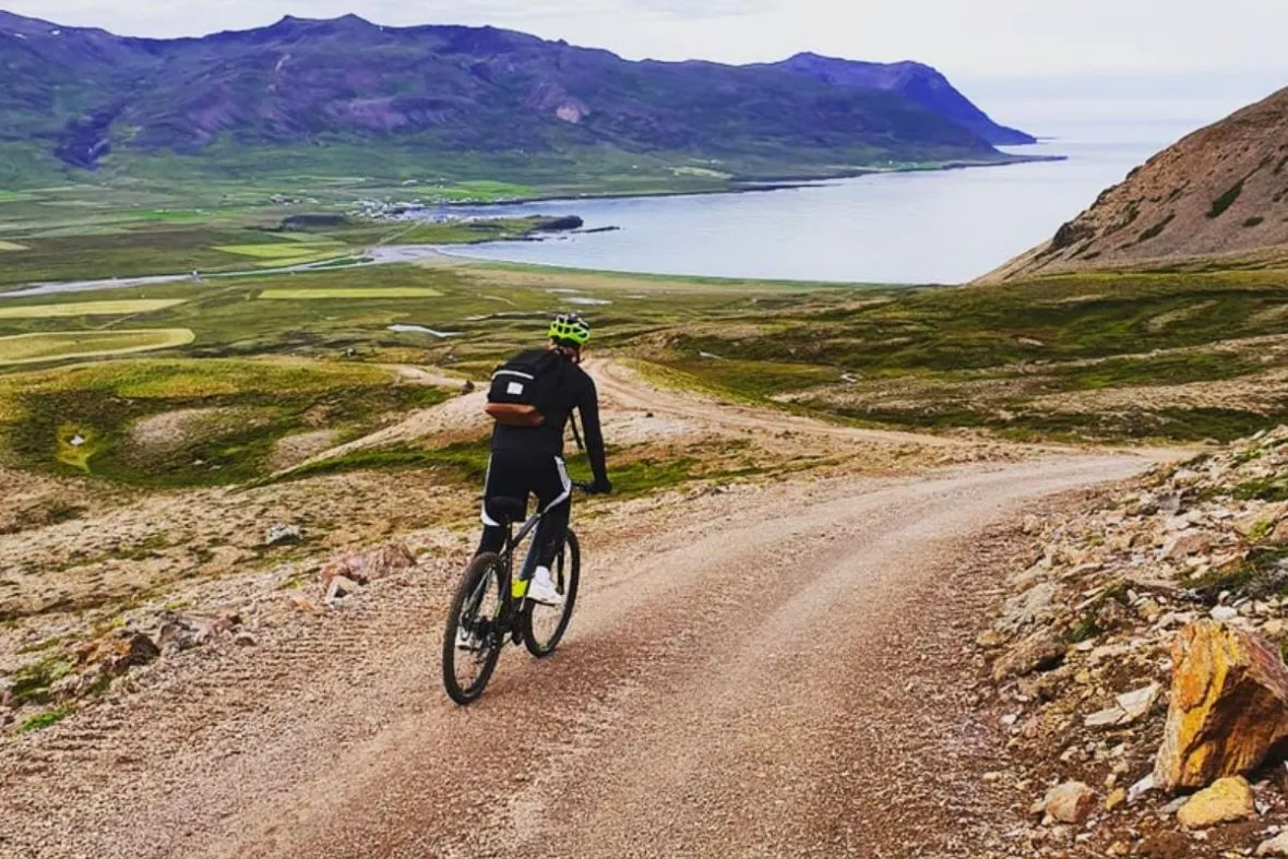 Cyclist riding down a gravel mountain trail toward the scenic coast in East Iceland.