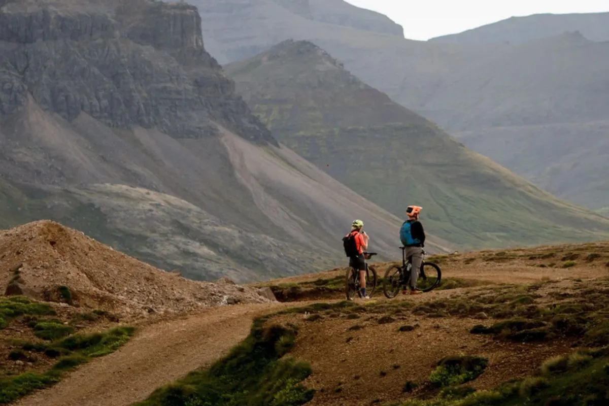 Two mountain bikers standing with their bicycles on a dirt path surrounded by rugged cliffs.