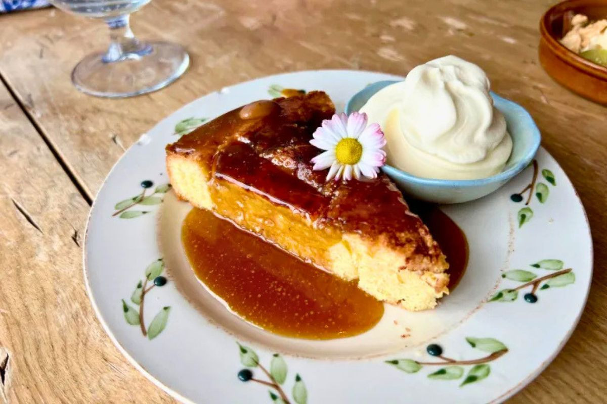 A slice of caramel-glazed cake served with a scoop of whipped cream and a small daisy flower at Vagninn- Pub & Bistro