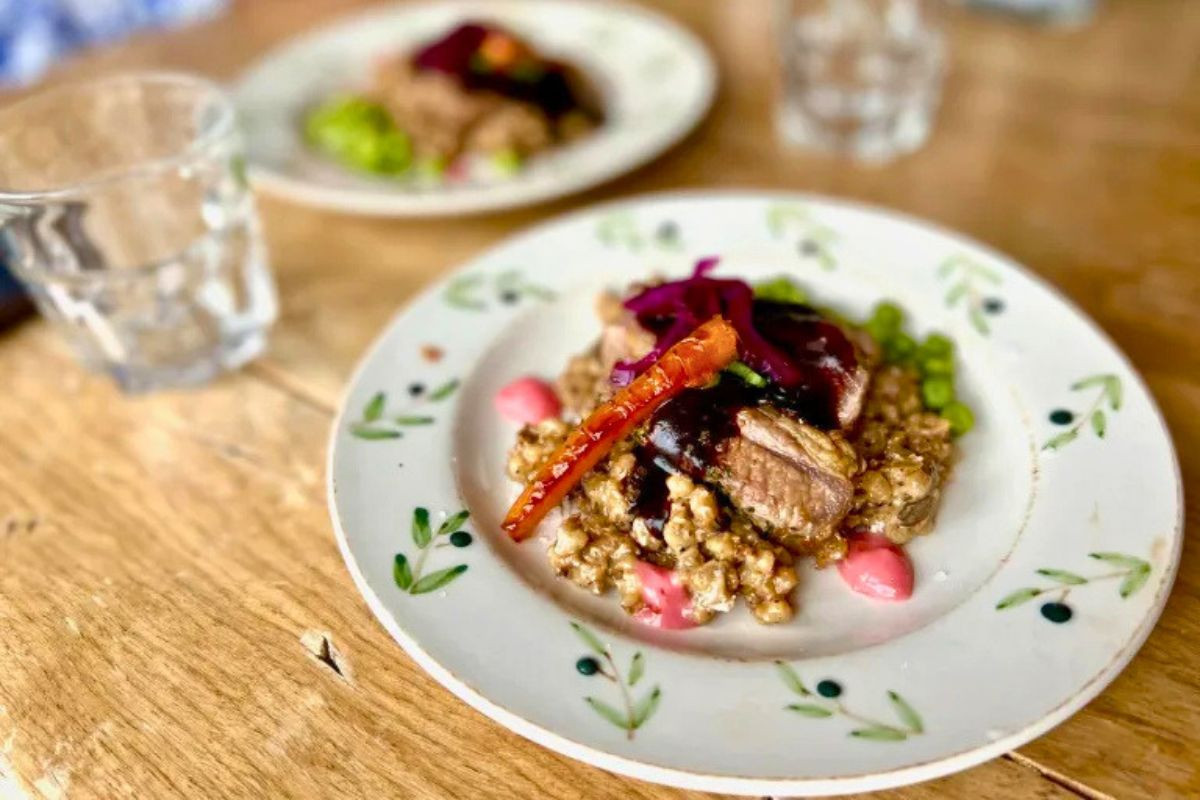 A gourmet plated meat dish with sauce, carrots, and peas at Vagninn Flateyri.
