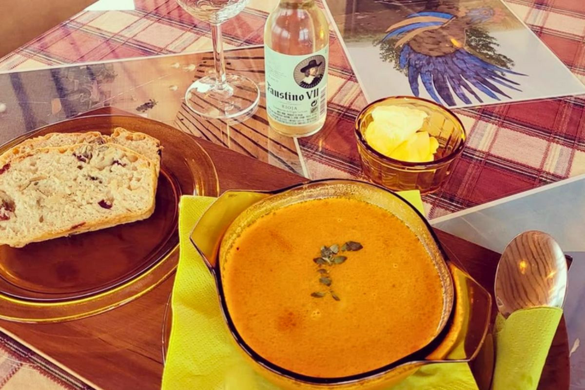 A bowl of creamy orange soup served with sliced bread and butter on a wooden platter at Hjá góðu fólki bistro.