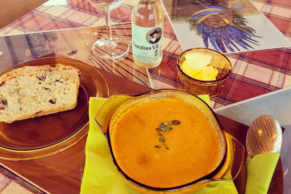 A bowl of creamy orange soup served with sliced bread and butter on a wooden platter at Hjá góðu fólki bistro.