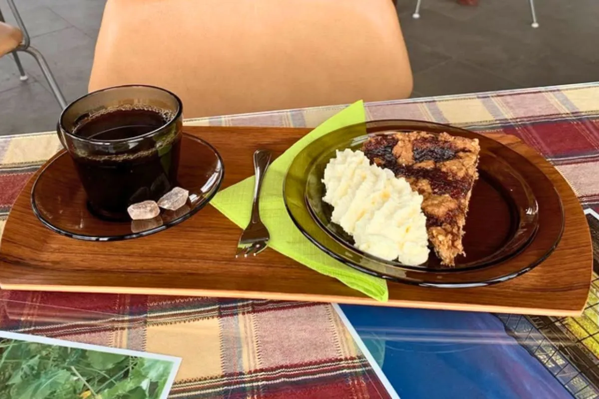 A slice of berry crumble pie with whipped cream next to a cup of black coffee at Hjá góðu fólki café.