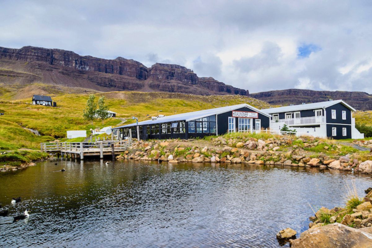 Hraunsnef Country Hotel and restaurant buildings next to a scenic pond below mountains.