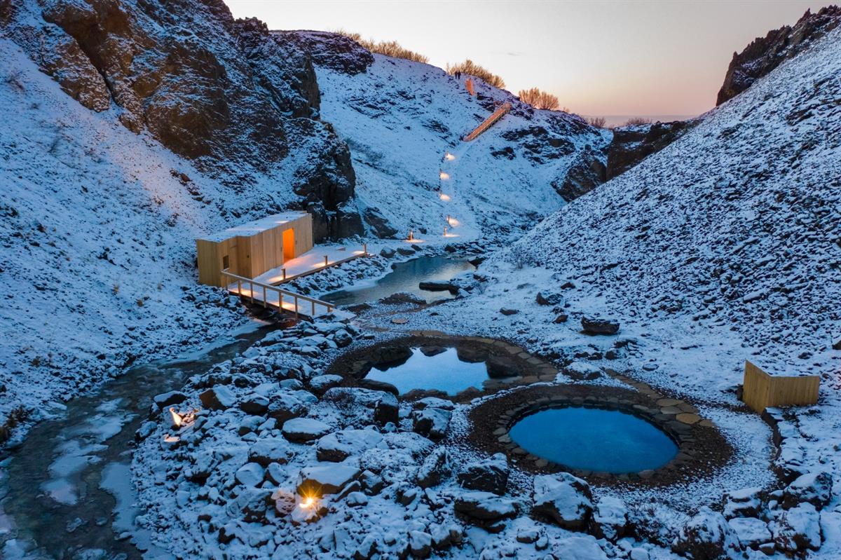 Evening view of the snow-covered Húsafell Canyon Baths and illuminated bathhouse in winter.