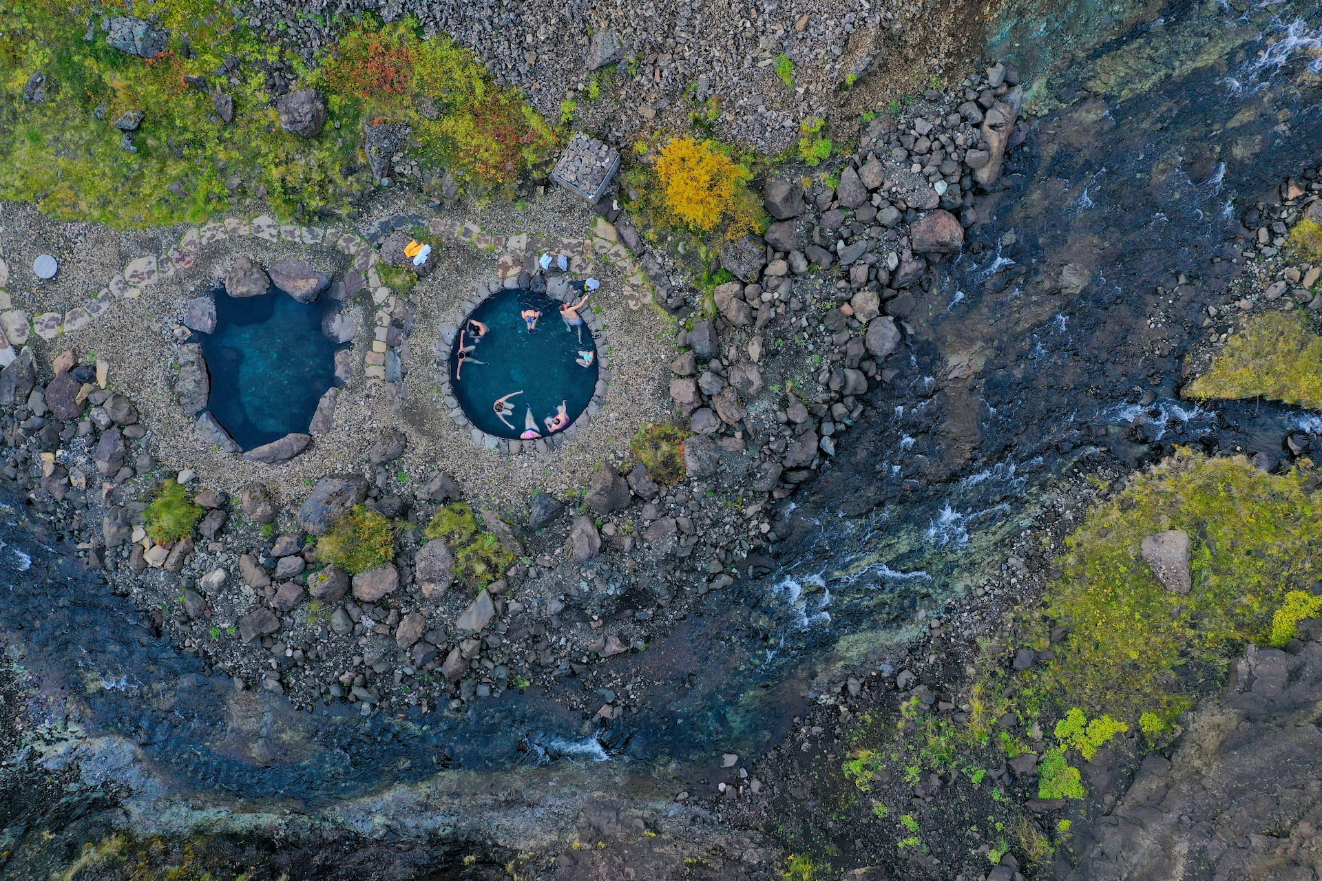 View of visitors bathing in the circular stone pools at Húsafell Canyon Baths.