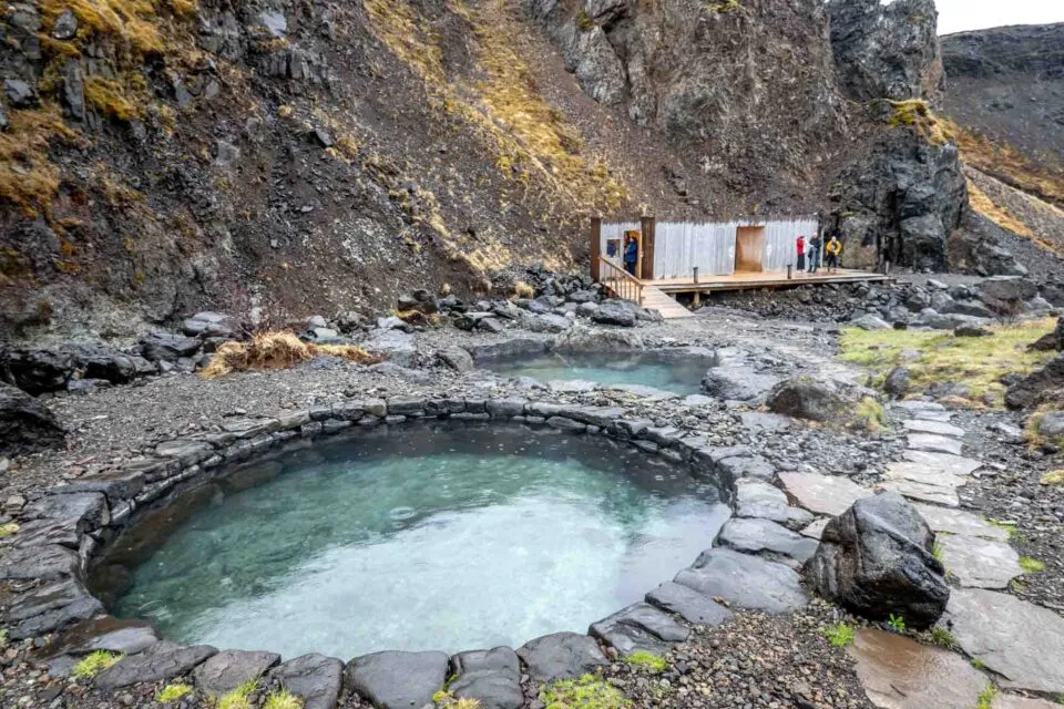 Clear geothermal stone pools next to a modern wooden changing facility at Húsafell Canyon Baths.