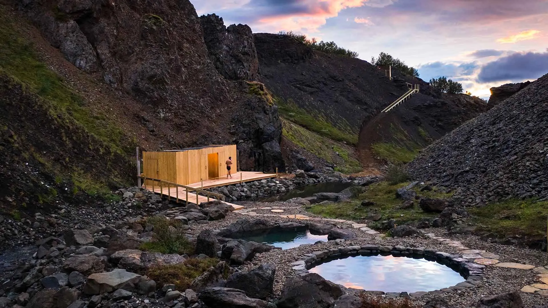 Scenic twilight view of the natural hot tubs at Húsafell Canyon Baths surrounded by rocky cliffs in West Iceland.
