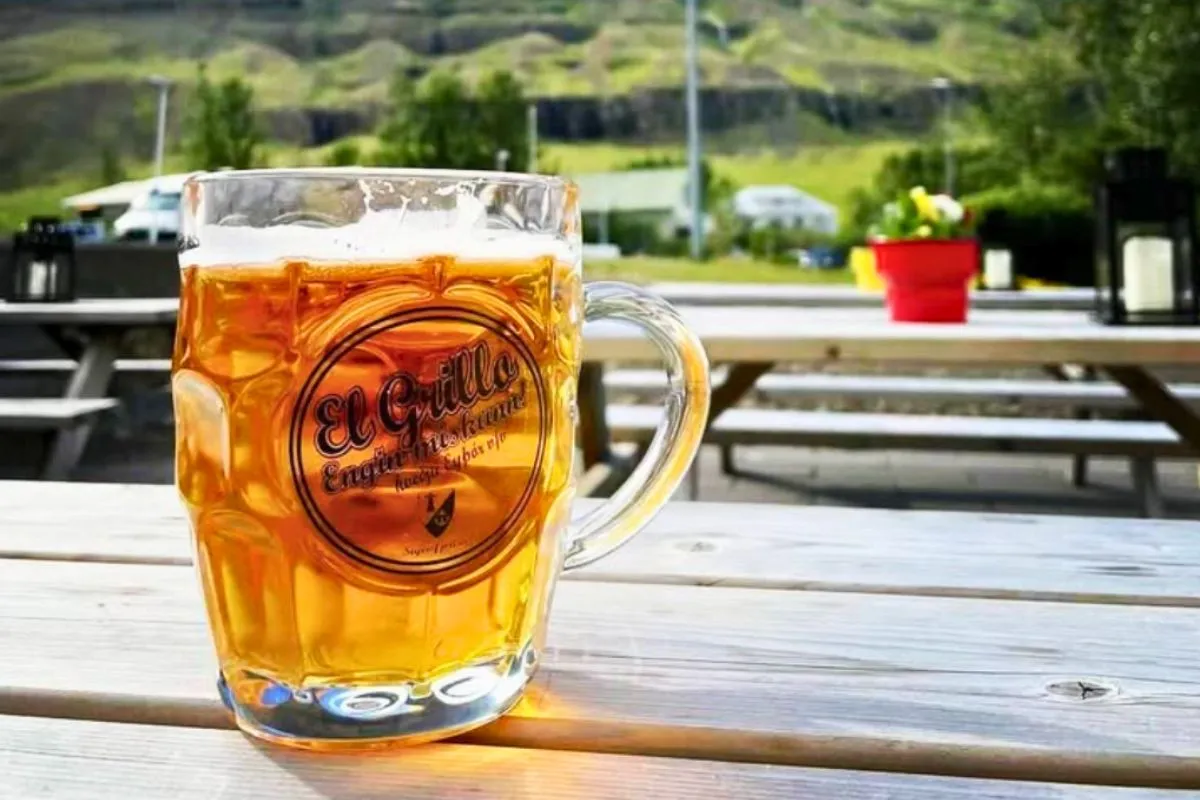 A glass mug of El Grillo beer on a wooden patio table at Kaffi Lára in Seyðisfjörður.