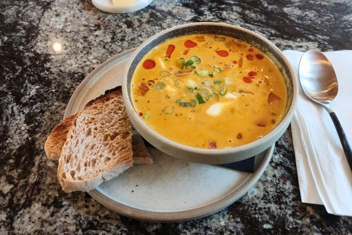 A bowl of creamy orange soup garnished with herbs and chili oil, served with crusty bread at LYST café.