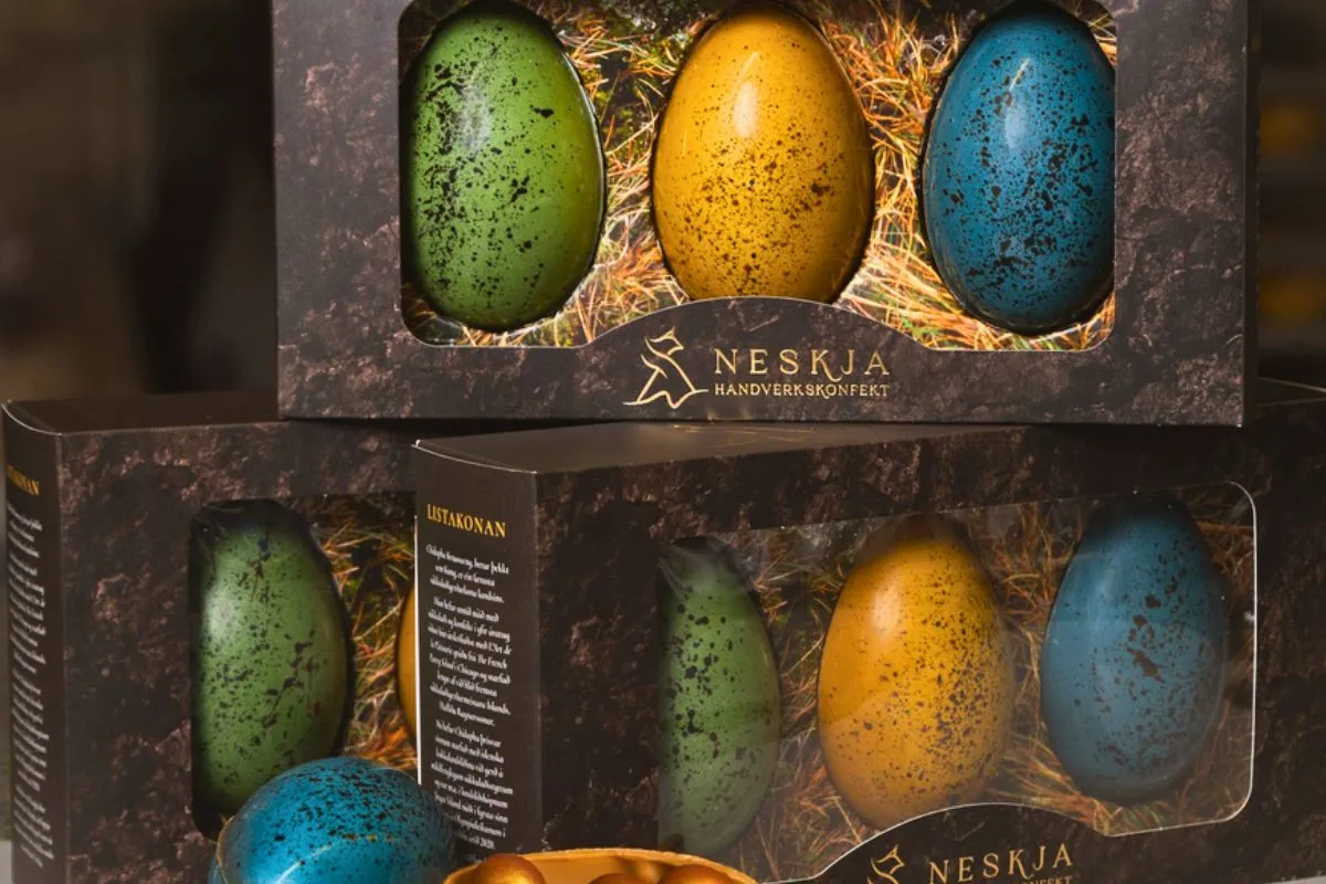 Stacked gourmet chocolate Easter egg gift boxes showcasing speckled green, yellow, and blue candy shells.