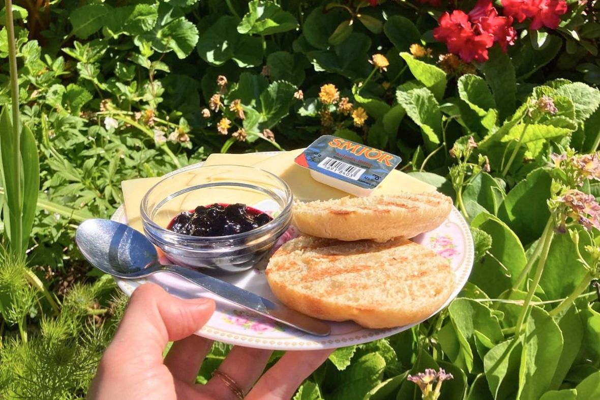 A plate of grilled bread rolls, jam, cheese, and Smjör Icelandic butter served in a lush green garden setting.