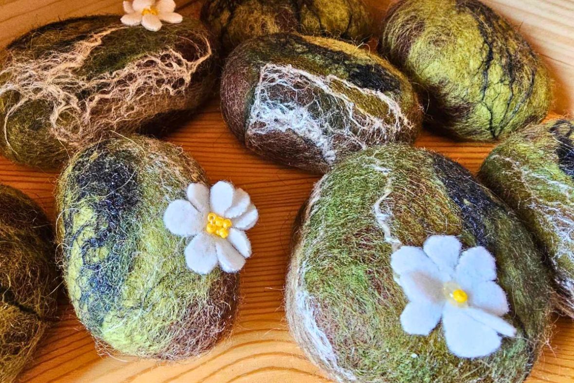 Decorative felted wool stones adorned with white fabric flowers on display at Stuðlagil – Local Craft.